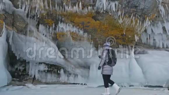 贝加尔湖冰上女子旅行去冬岛旅行女孩走在冰岩脚下旅行者看着视频的预览图