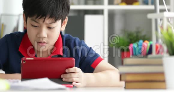 快乐的亚洲男孩在家里微笑着看着平板电脑视频的预览图