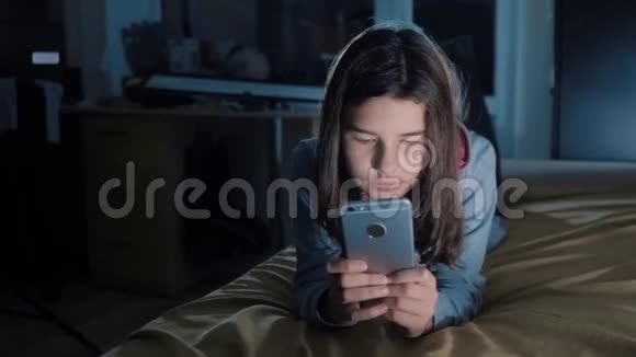年轻女孩网上购物在晚上的生活方式中在床上看她的智能手机一个小少女写的视频的预览图