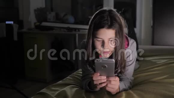 十几岁的女孩网上购物在晚上的生活方式中在床上看她的智能手机一个小少女写的视频的预览图