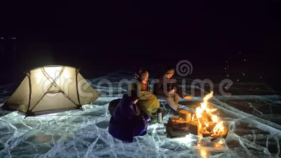 夜间有三个乘火的旅行者在冰上在冰上露营帐篷就在火旁边贝加尔湖就在附近视频的预览图