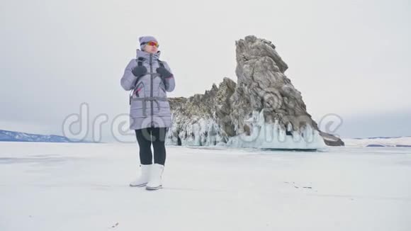 贝加尔湖冰上女子旅行去冬岛旅行女孩走在冰岩脚下旅行者看着视频的预览图