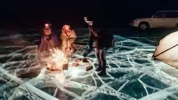 三个旅行者在夜晚的冰面上露营地冰帐篷站在火堆旁边人们是视频的预览图