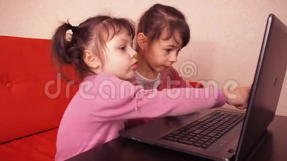 孩子们在笔记本电脑里玩两个小女孩印在笔记本电脑上两个姐姐坐在橙色的沙发上看着一圈视频的预览图