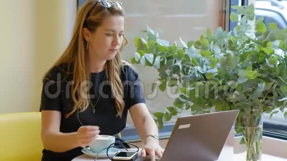 商务女性坐在咖啡馆的桌子旁喝咖啡在笔记本电脑上工作视频的预览图