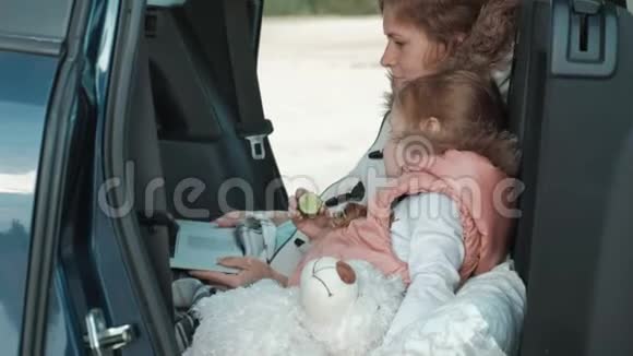 美丽的年轻女子和她的小女儿正坐在海边的一辆敞篷汽车的后备箱里视频的预览图