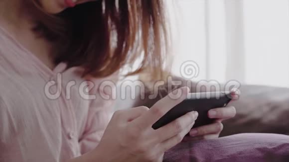 快乐的亚洲女人早上在床上使用智能手机视频的预览图