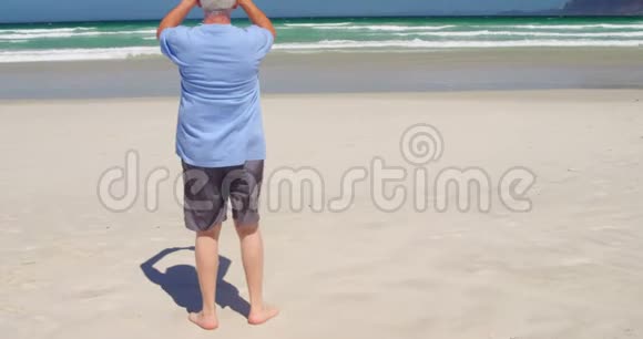 在海滩上用手机拍照的老人视频的预览图