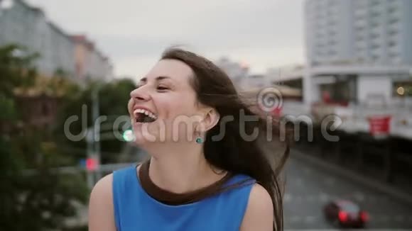 风吹长黑发美丽的年轻女人快乐微笑的女孩站在桥上看着摄像机视频的预览图