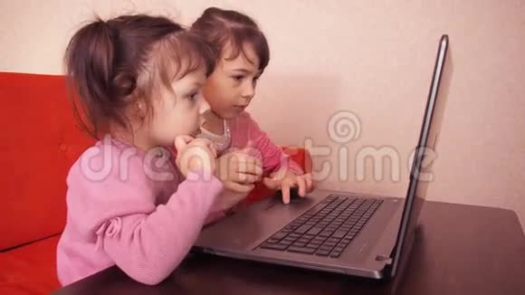 孩子们在笔记本电脑里玩两个小女孩印在笔记本电脑上两个姐姐坐在橙色的沙发上看着一圈视频的预览图