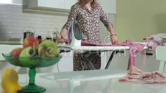 女人在厨房的家里熨一大堆衣服视频的预览图