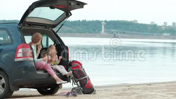 美丽的年轻女子和她的小女儿正坐在一条海边的一辆敞篷汽车的后备箱里视频的预览图