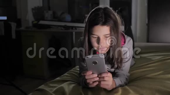十几岁的女孩网上购物在床上看智能手机小青少年生活方式帽女孩写视频的预览图