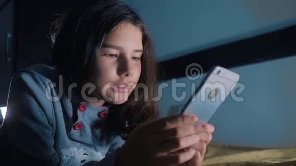十几岁的女孩晚上在床上看她的智能手机一个小女孩在社交中写了一条聊天信息视频的预览图