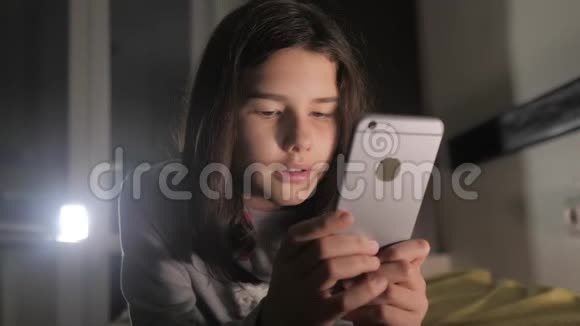 十几岁的女孩在网上购物时晚上在床上看她的生活方式智能手机一个小少女写的视频的预览图