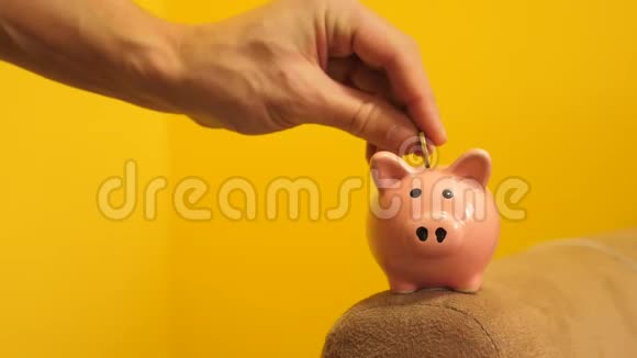 猪银行的经营理念一只手把生活方式的硬币放在黄色背景的储蓄罐里省钱就是视频的预览图