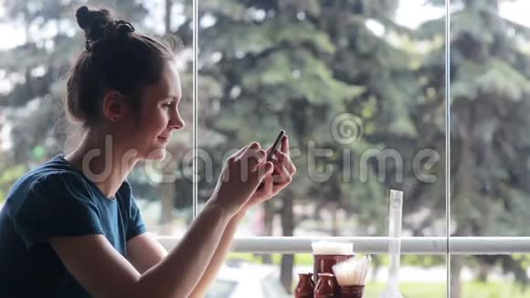 坐在窗户附近使用智能手机的女人视频的预览图