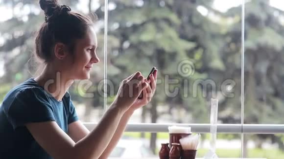 坐在窗户附近使用智能手机的女人视频的预览图