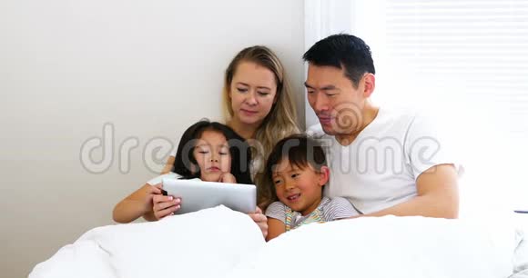 快乐的家庭在床上放松使用数码平板电脑视频的预览图