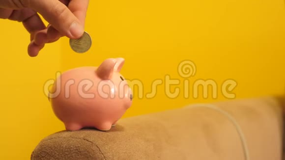 猪银行的经营理念一只手把硬币放在黄色背景下的储蓄罐生活方式中省钱就是视频的预览图