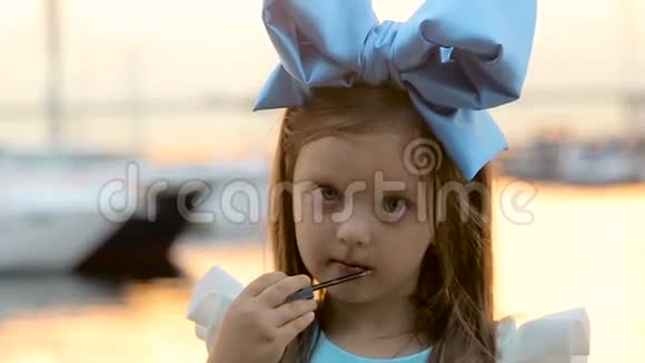 一个小女孩的肖像头上戴着蓝色的蝴蝶结站在水边视频的预览图