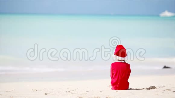 圣诞节假期戴着圣诞帽的小可爱女孩在白海滩度假视频的预览图