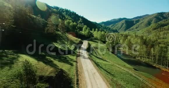 空中UHD4K视野阳光明媚的夏天低空飞越山区乡村土路和草地视频的预览图