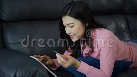 幸福的女人用数字平板电脑上网购物客厅里有信用卡视频的预览图