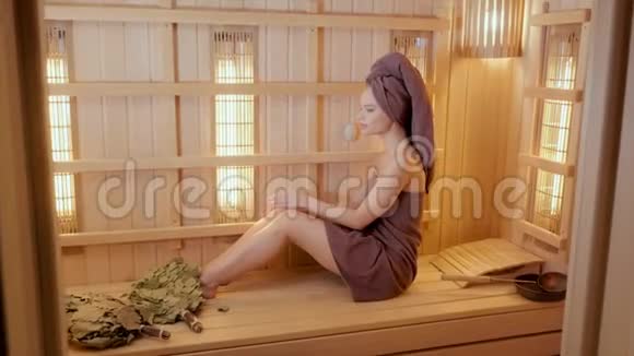 年轻女子穿着毛巾在桑拿浴室里放松新芬兰桑拿浴室内部医疗用红外线面板视频的预览图