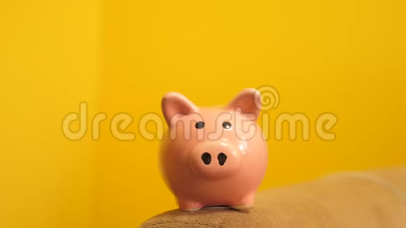 猪银行的经营理念一只手把硬币放在黄色背景上的储蓄罐里节省生活方式的钱视频的预览图