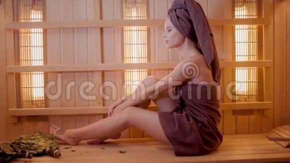 年轻女子穿着毛巾在桑拿浴室里放松新芬兰桑拿浴室内部医疗用红外线面板视频的预览图