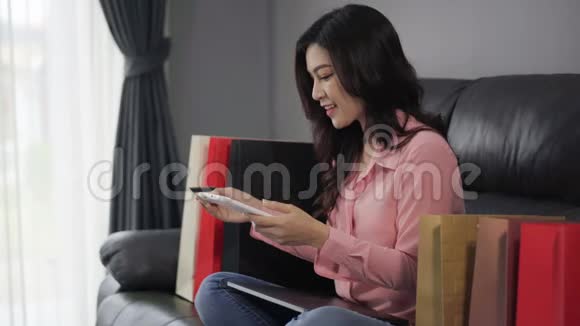 幸福的女人用数字平板电脑上网购物客厅里有信用卡视频的预览图