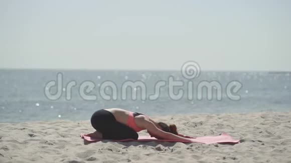 阳光明媚的一天年轻漂亮的女人在海滩上练习瑜伽健康的积极生活方式视频的预览图