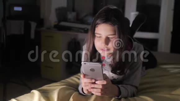 十几岁的女孩网上购物在床上看她的智能手机一个小女孩写了一条信息视频的预览图