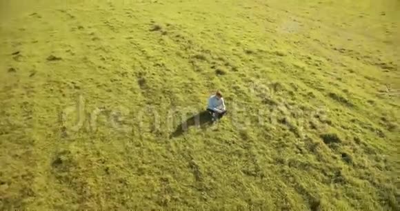 超高清4k鸟瞰图低轨道飞行超过商人坐在草地上带笔记本垫在野外视频的预览图