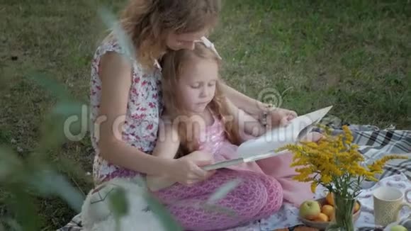 一对幸福的母女在相册里看照片读一本书一家人在城市公园野餐在温暖的晚上视频的预览图
