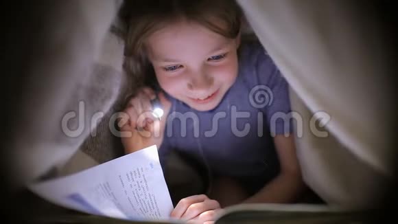小女孩正在一个黑暗的房间里用手电筒在毯子下面看书视频的预览图