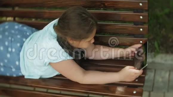 一个夏天一个小胖女孩坐在长凳上听音乐或看视频带着平板电脑和耳机视频的预览图