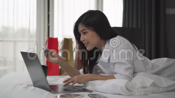 快乐的女人用笔记本电脑上网购物床上有信用卡视频的预览图