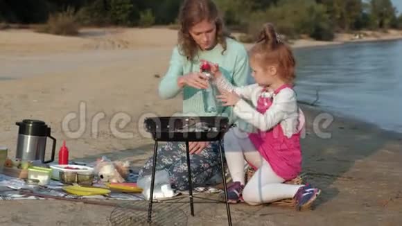 母亲和女儿在海滩上的烧烤上煎肉和蔬菜视频的预览图