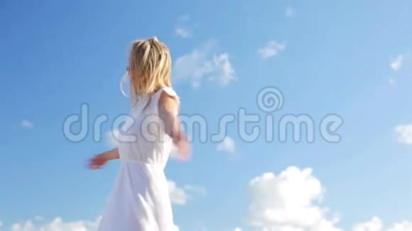 穿着白色衣服在蓝天上微笑的年轻女子视频的预览图
