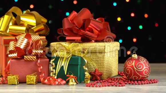 漂亮的圣诞礼物盒和装饰在木地板上在黑色背景上五颜六色的闪光花环上视频的预览图