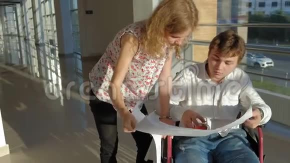 一位坐在轮椅上的残疾商人在窗户上一张大纸上写着一张照片与一位同事讨论工作视频的预览图