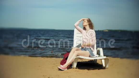 年轻女孩躺在海边沙滩上的躺椅上晒太阳视频的预览图