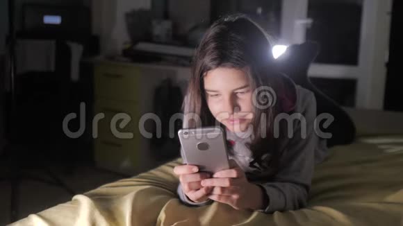 十几岁的女孩网上购物在床上看她的智能手机一个小女孩写了一条信息视频的预览图