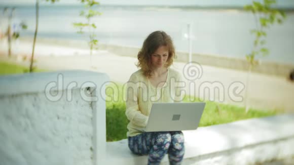 美丽的女人在公园的木凳上用笔记本电脑工作视频的预览图