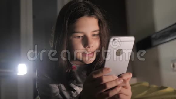 十几岁的女孩在网上购物的生活方式看她的智能手机在床上过夜一个小少女写的视频的预览图