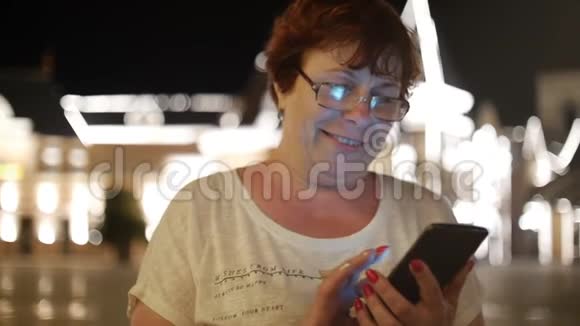 在一个夜晚的城市里女人用手机穿过街道在背景的夜晚城市里视频的预览图
