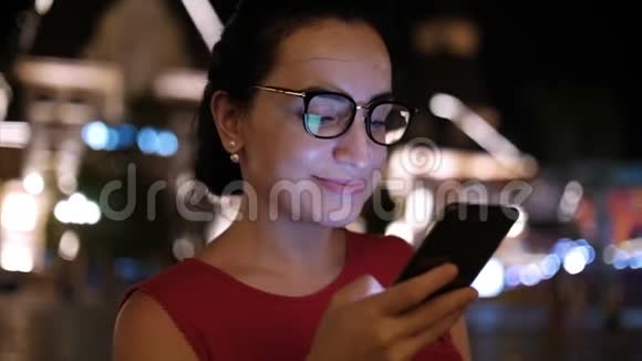 有魅力的女人在夜城的街道上在背景的夜城里用手机穿过街道视频的预览图