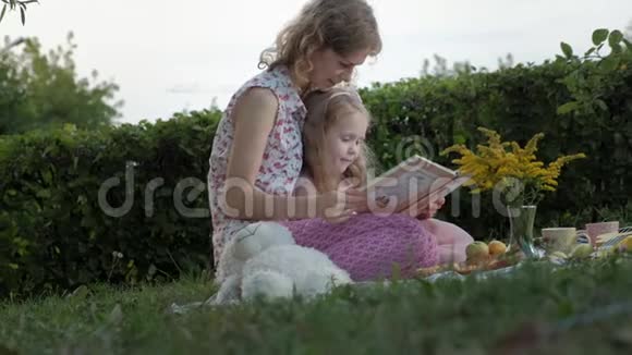 一对幸福的母女在相册里看照片读一本书一家人在城市公园野餐在温暖的晚上视频的预览图